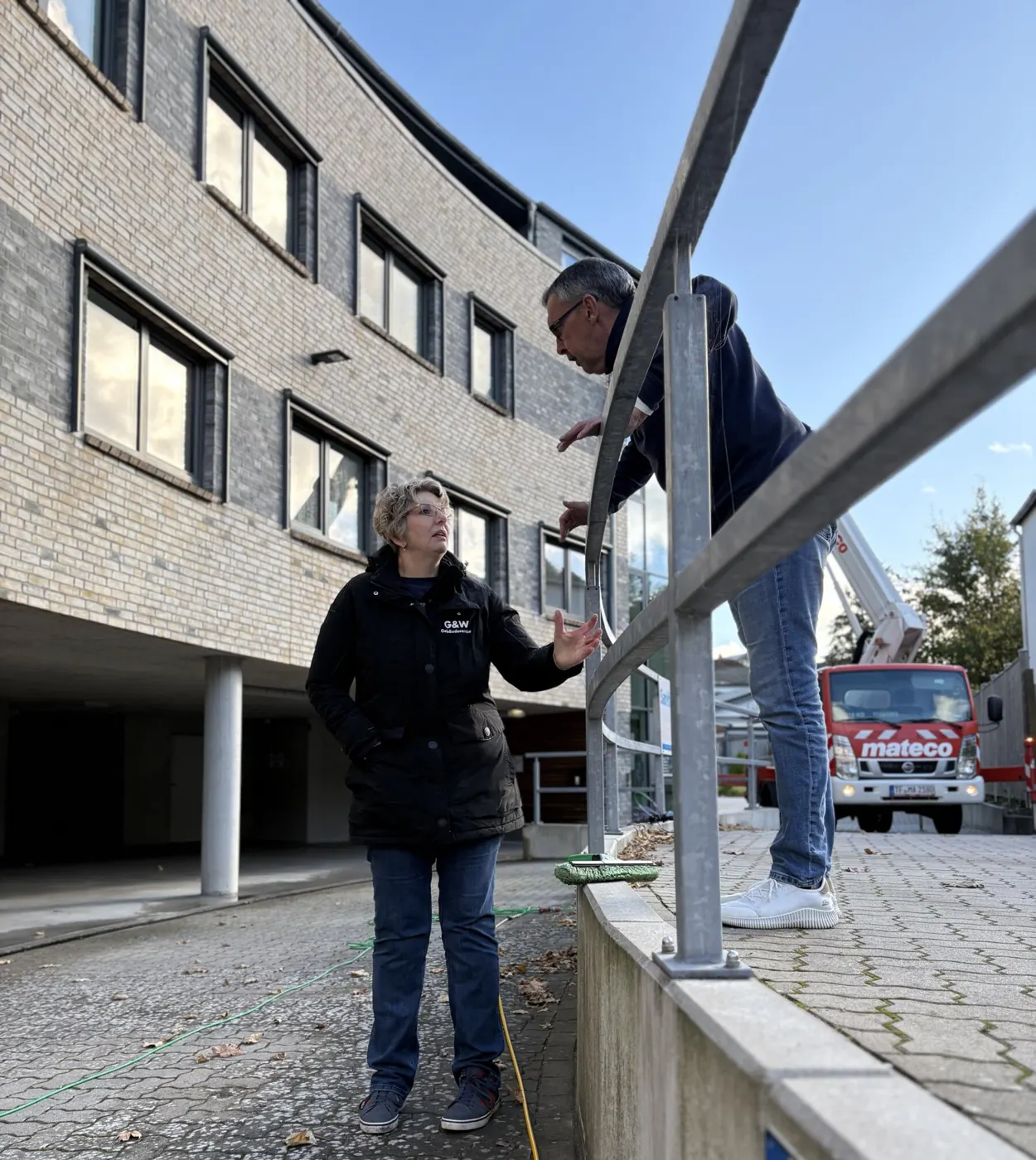 Die Inhaber von G&W bei der Arbeit vor einem Bürogebäude, im Hintergrund eine Hebebühne.
