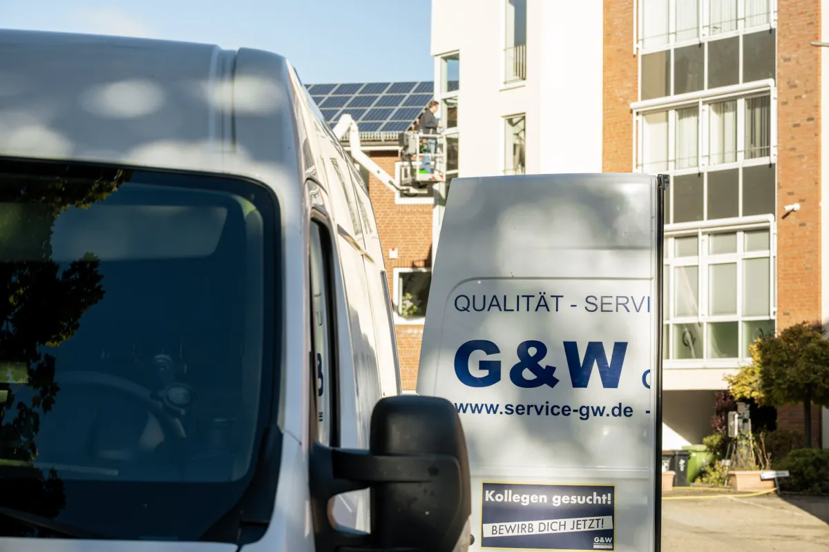Das Heck eines weißen G&W-Transporters mit dem Aufkleber Kollegen gesucht, bewirb dich jetzt, im Hintergrund eine Hebebühne.