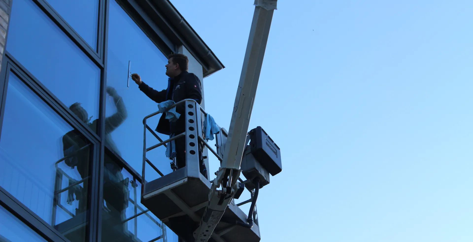 Ein Mitarbeiter von G&W reinigt von einer Hebebühne aus die Glasfassade eines Bürogebäudes, dahinter blauer Himmel.