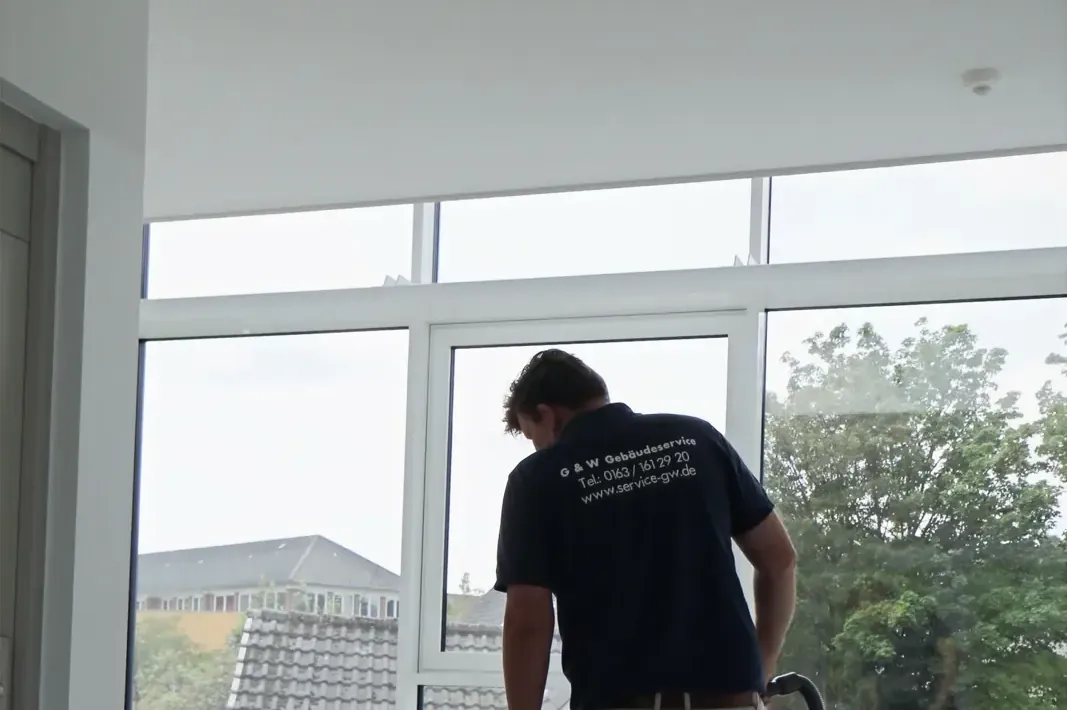 Ein Mitarbeiter von G&W im Firmenshirt reinigt den Boden eines hellen Flurs mit großen Fenstern.
